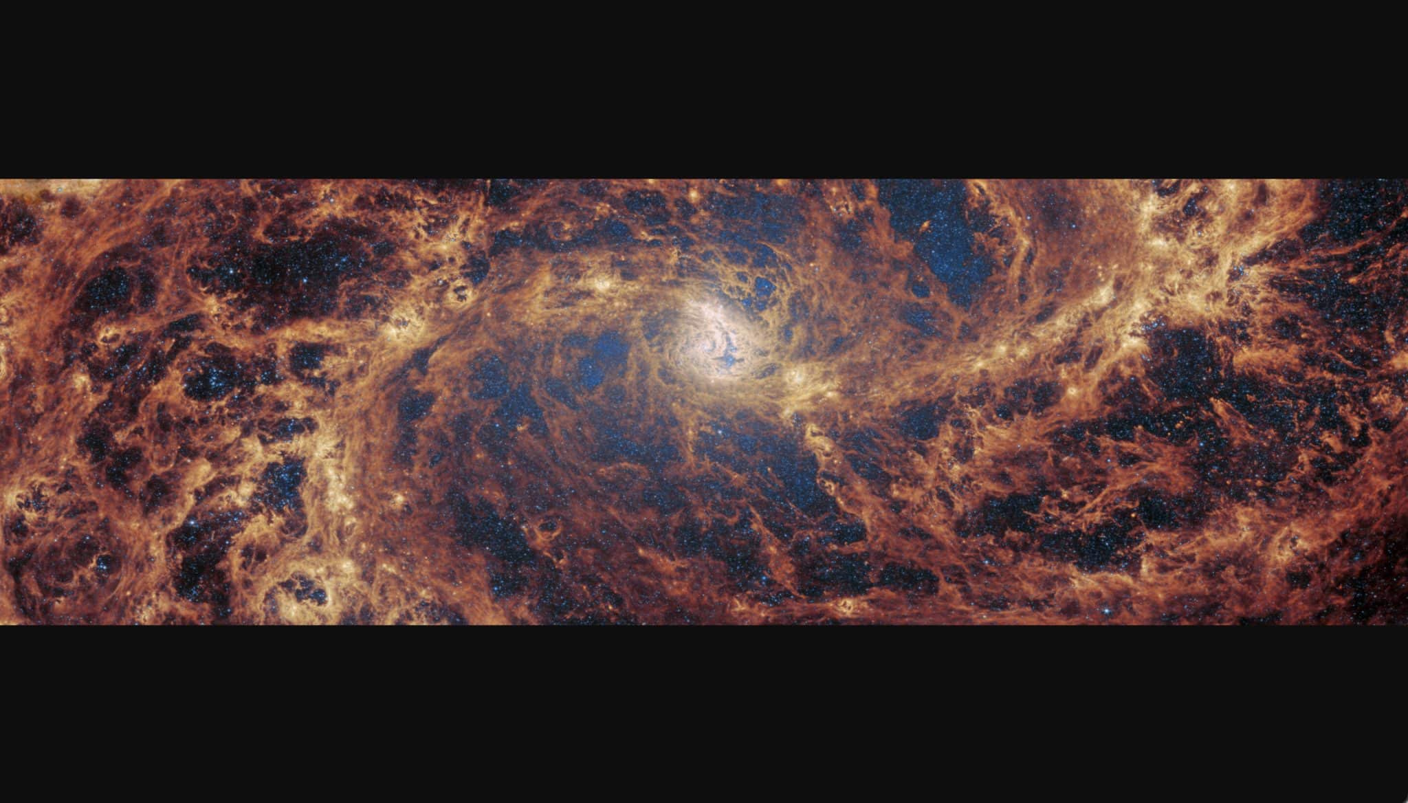 Изображение Южной Вертушки (М83) крупным планом: два спиральных рукава, горизонтально отходящих от ядра в центре, сливаются в широкую сеть из газа и пыли и заполняют пространство. Ярко-оранжевым светится вещество вдоль рукавов, а темно-красным — по всей части галактики. / ©  ESA/Webb, NASA & CSA, A. Adamo (Stockholm University) and the FEAST JWST team