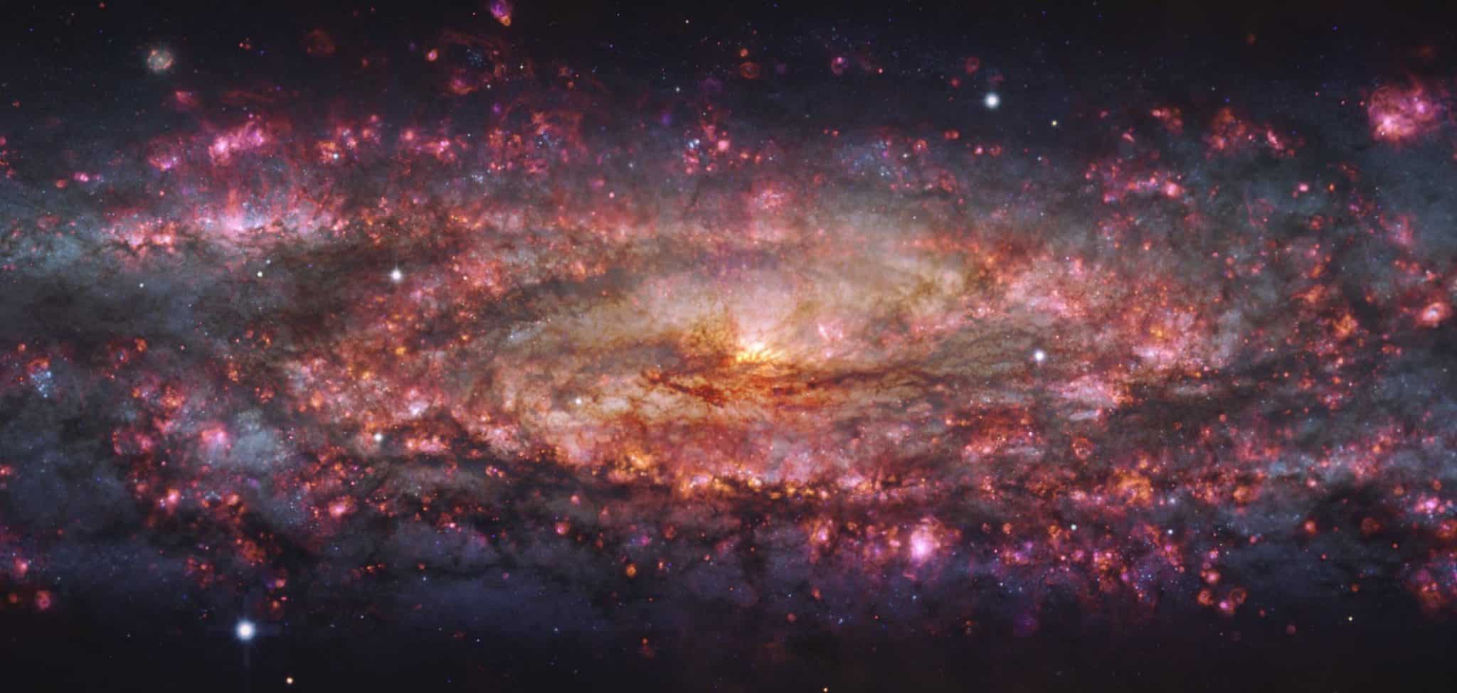 Снимок-«мозаика» галактики Скульптор, составленный из снимков, сделанных инструментом MUSE телескопа VLT в разных диапазонах волн. Розовым «светится» ионизированный водород в областях звездообразования. В видимом диапазоне мы это излучение не видим / © ESO/E. Congiu et al.